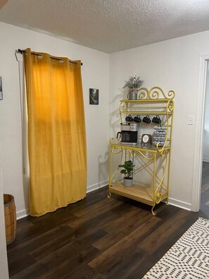 A room with a yellow curtain, a yellow metal shelf with items, and a wooden floor.