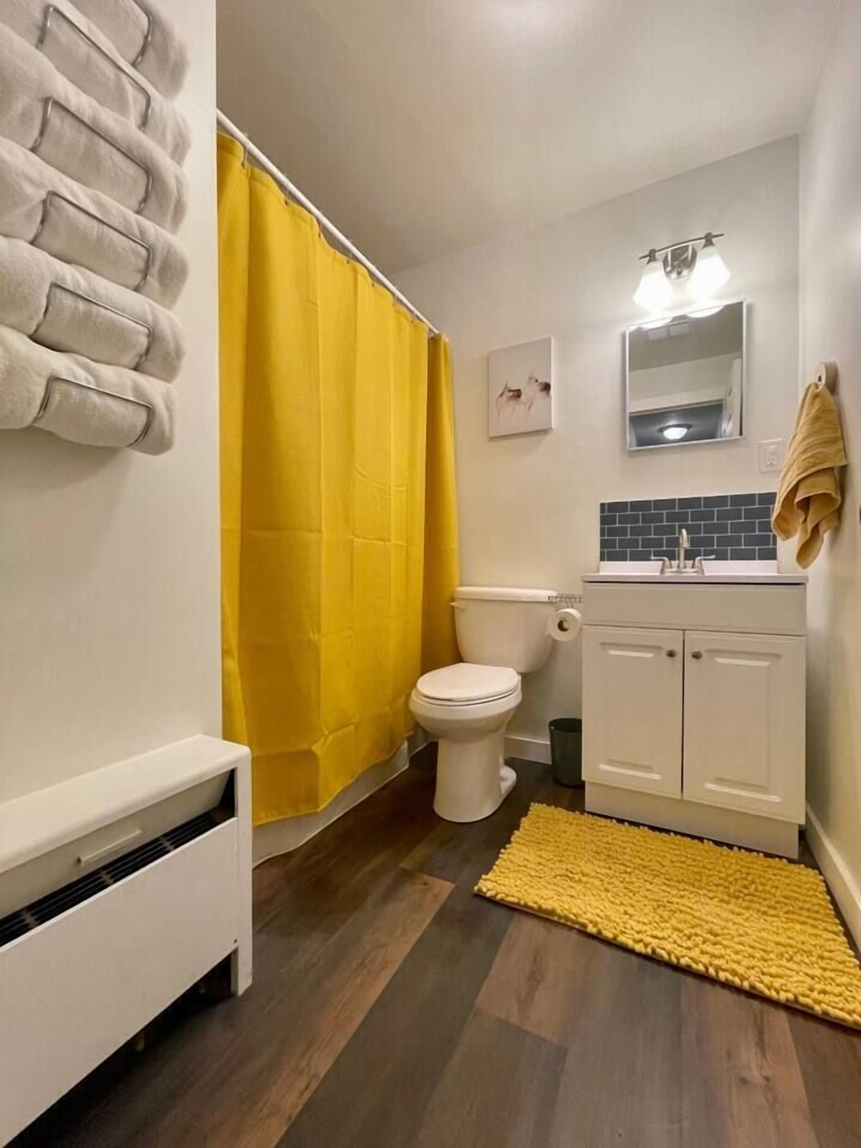 Et badeværelse med toilet, vask, spejl og en gul badegardiner.