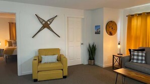Un salon avec un canapé jaune, un canapé gris, une table basse en bois, une plante en pot et un élément décoratif fixé au mur.