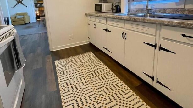 Une cuisine avec des meubles blancs, un four à micro-ondes et un tapis à motifs.