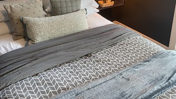 Een slaapkamer met een bed, kussens, een nachtkastje, een hanglamp en een lijst met een afbeelding aan de muur.