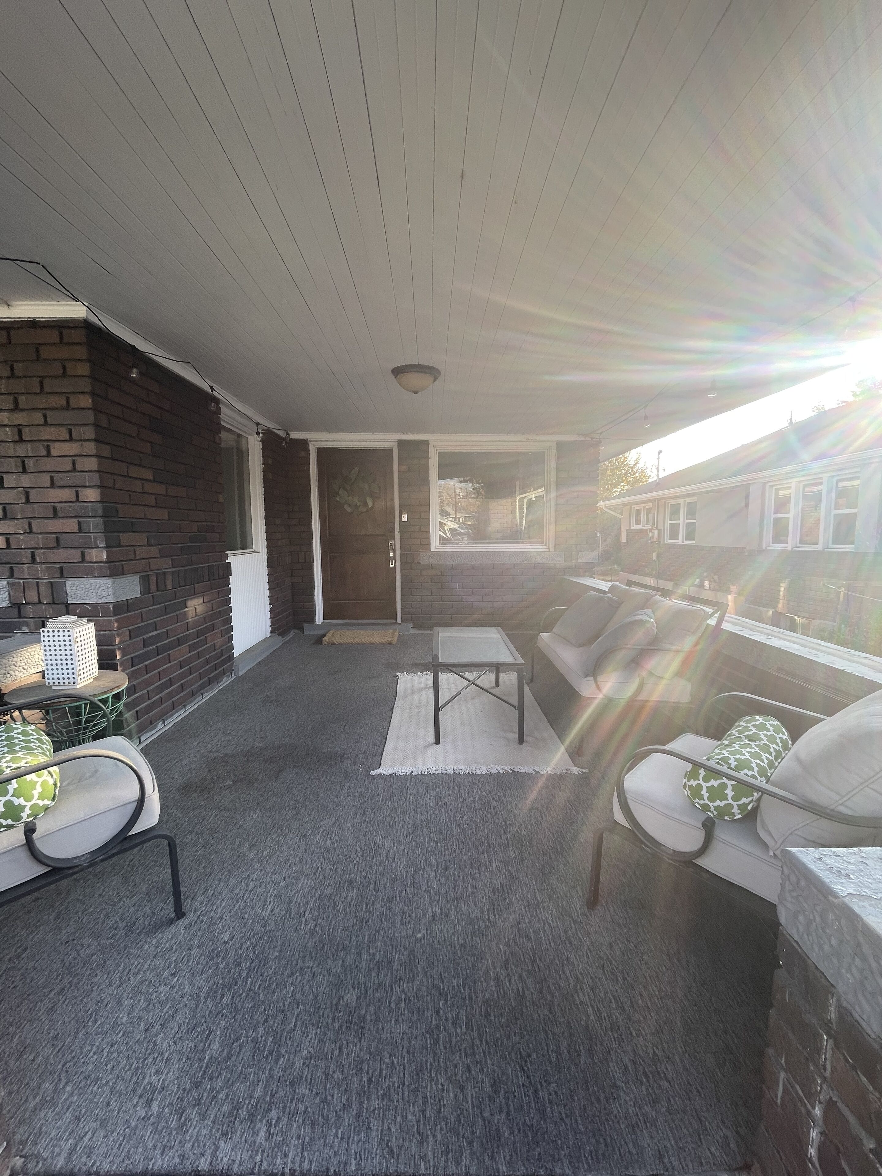 A covered patio area with a brick wall, a glass door, and a seating arrangement including a table and chairs.