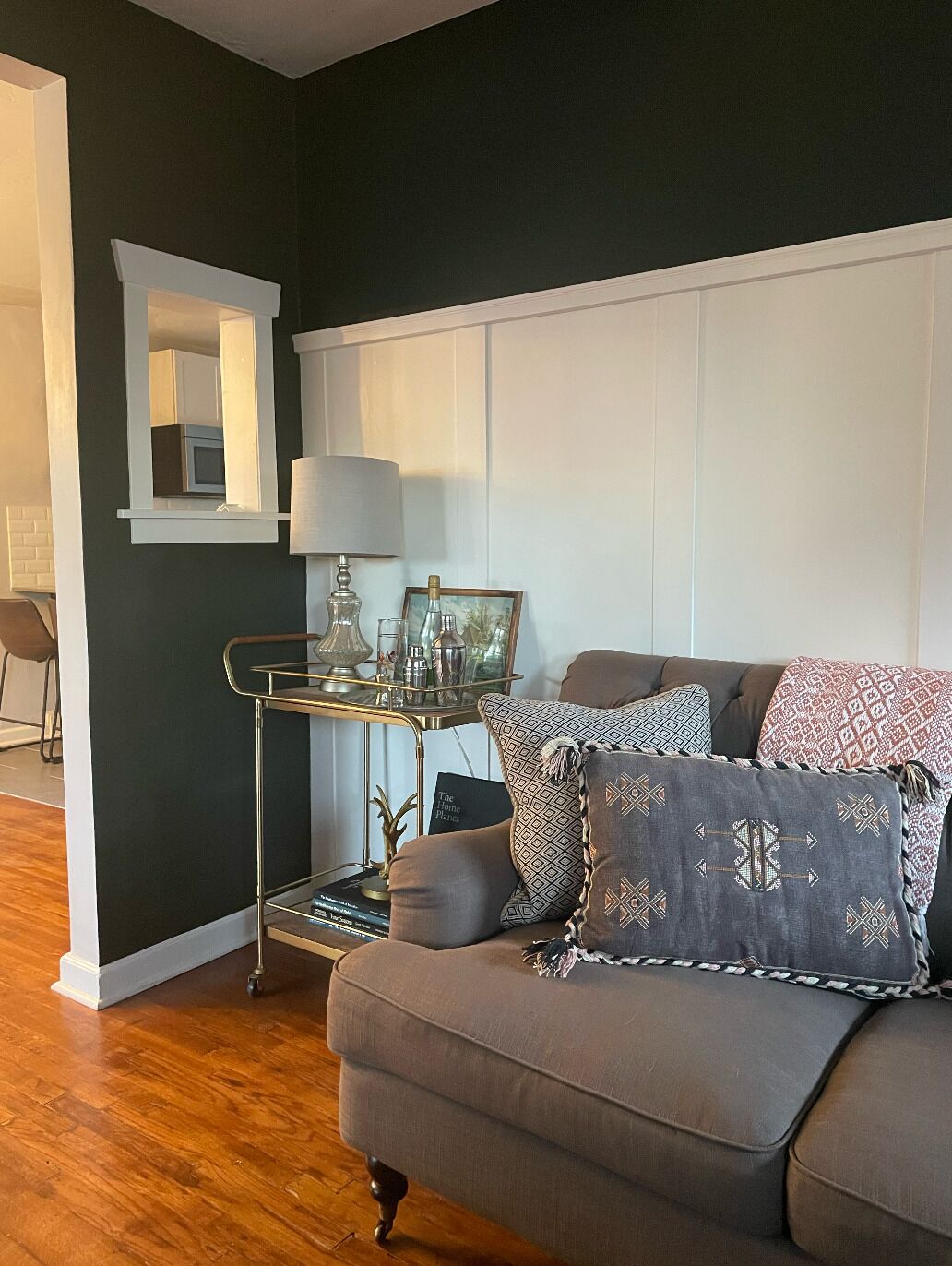 A living room with a grey sofa, a small side table with decorative items, a mirror, and a bookshelf.