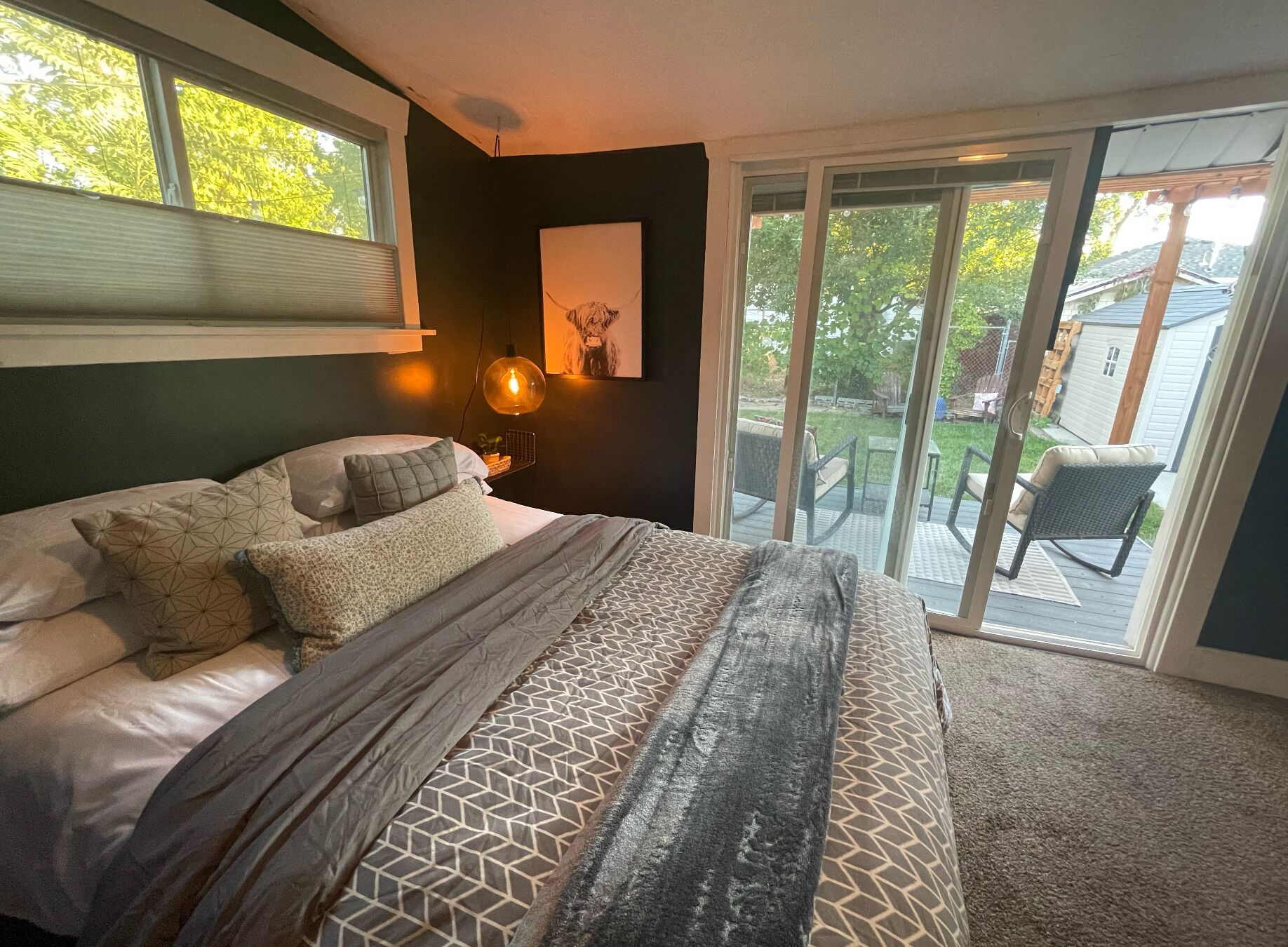 Une chambre à coucher comprenant un lit, une grande fenêtre, une porte-fenêtre coulissante donnant sur une terrasse et un luminaire fixé au mur.