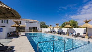A swimming pool with lounge chairs and umbrellas, surrounded by buildings with white walls and tiled roofs. - Studio Abordable et Cosy, à 5 minutes de la plage (Rivedoux-Plage)