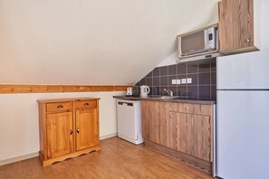 Eine kompakte Küche mit Holzausstattung, einer Mikrowelle, einem Wasserkocher und einem Geschirrspüler.