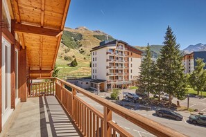 Ein Holzbalkon mit Blick auf einen Parkplatz, im Hintergrund Berge.
