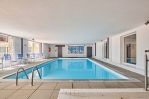 An indoor swimming pool with clear blue water, surrounded by white walls and a tiled floor.