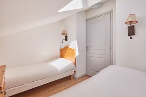 A bedroom with two single beds, a wooden headboard, a white door, and a wall-mounted lamp.