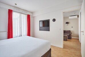 Una camera d'albergo con un letto, una TV a muro, un divano e un tavolino.