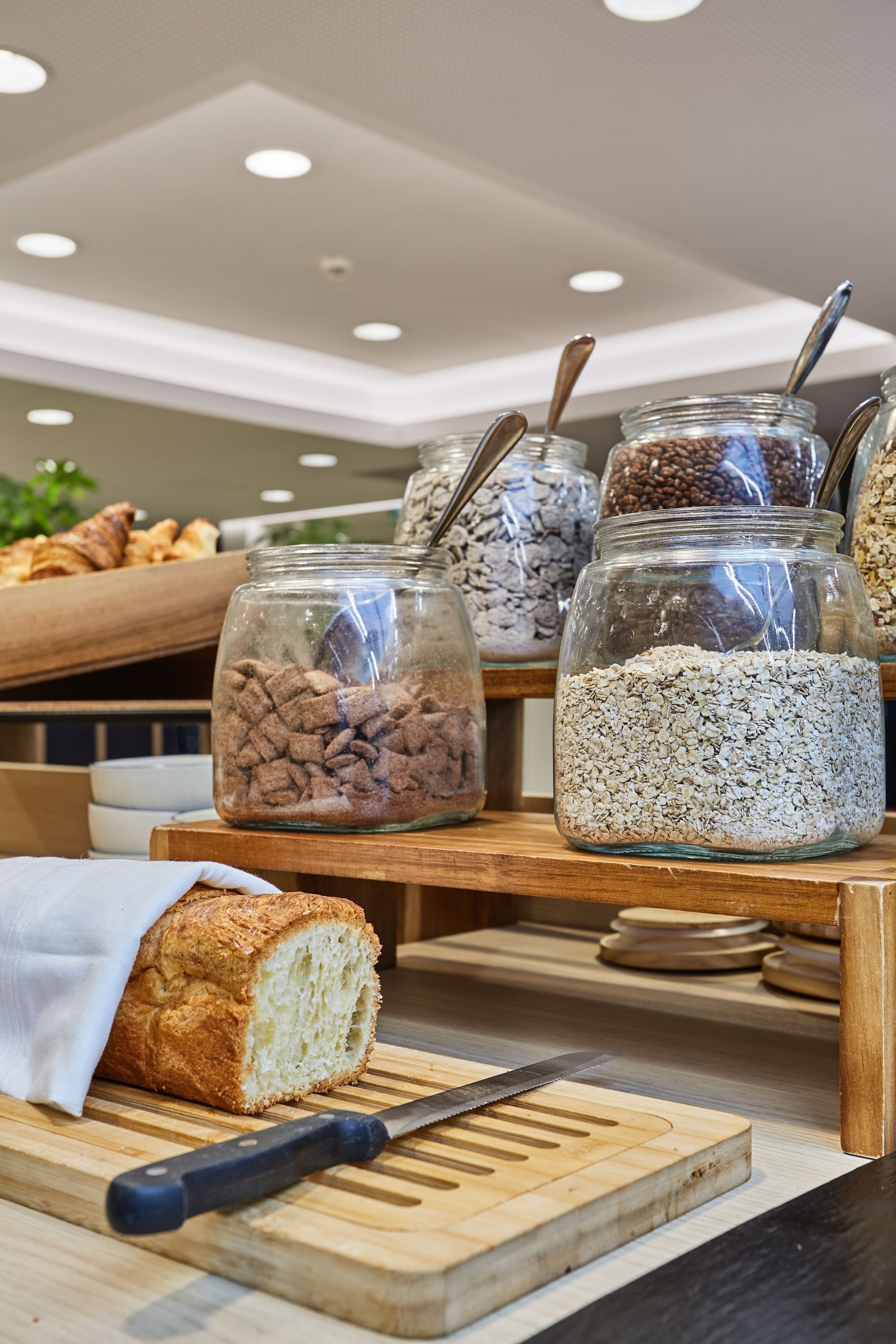 Une vitrine de boulangerie présentant des bocaux de granola et des biscuits, une miche de pain et une planche à découper avec un couteau.