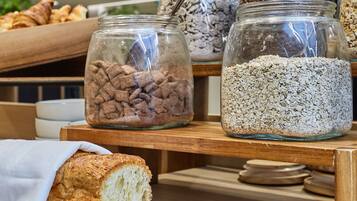 Une vitrine de boulangerie présentant des bocaux de granola et des biscuits, une miche de pain et une planche à découper avec un couteau.