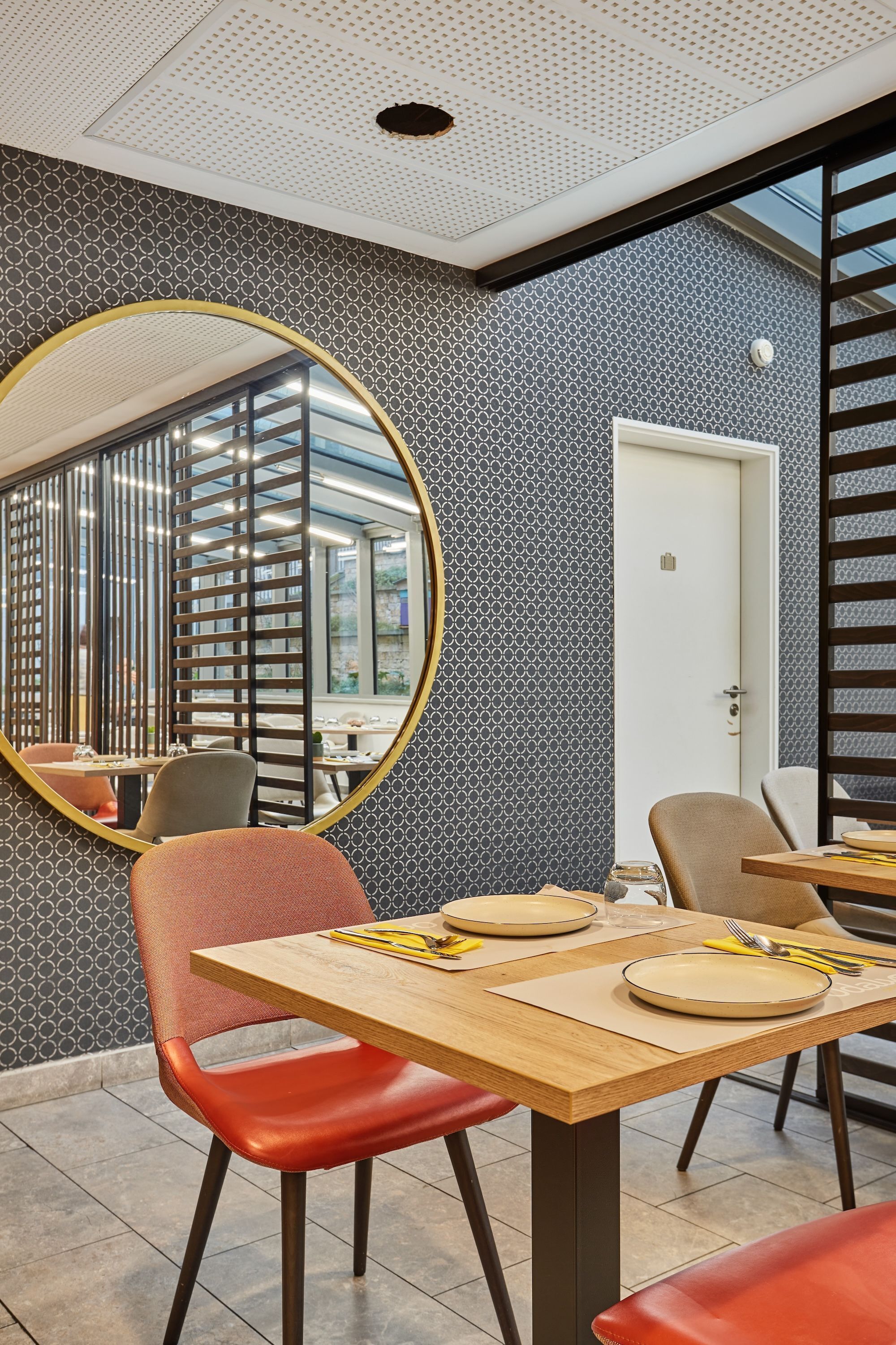 A dining area with a round mirror, a wooden table, and red chairs.