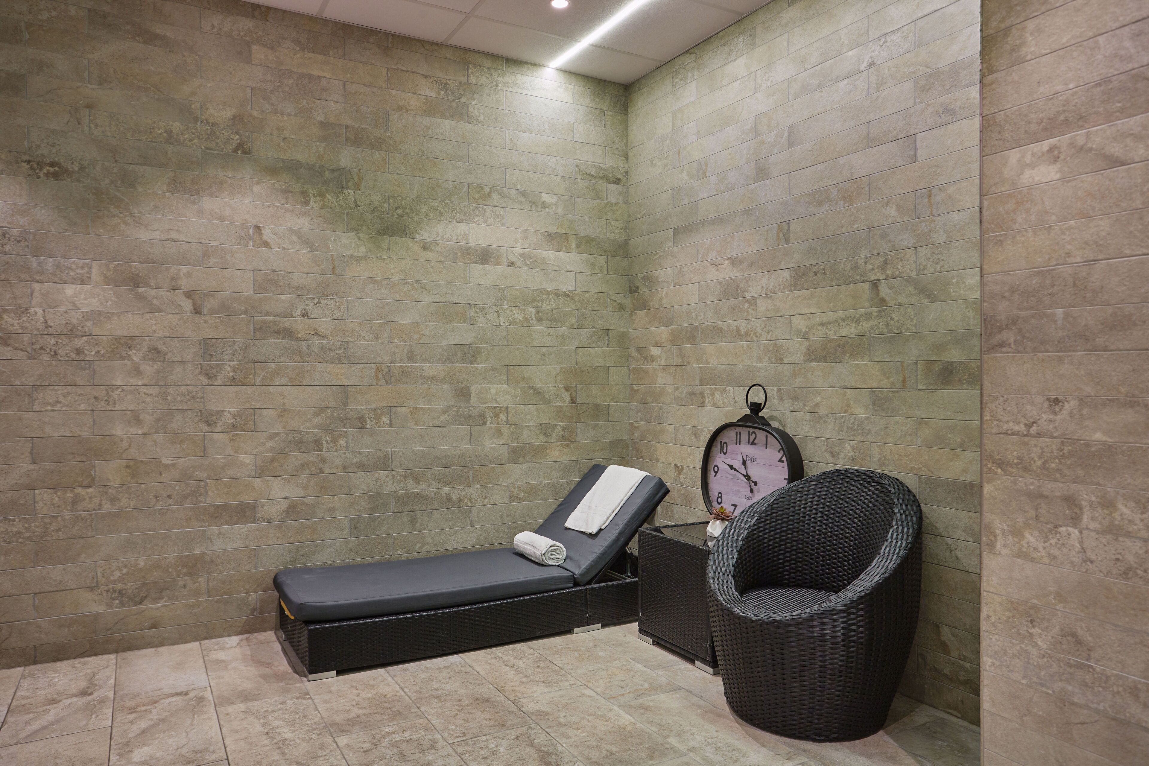 Een spa-ruimte met een massagetafel, een klok en een rieten stoel.