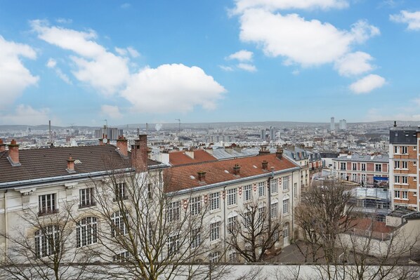 A cityscape with historic buildings, a clear sky, and distant industrial structures.