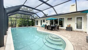 Une piscine entourée de parois en verre, un espace patio avec une table et des chaises, et une buanderie.