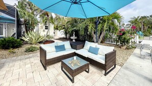 Un espace patio aménagé avec un canapé d’angle, une table basse et un grand parasol bleu offrant de l’ombre.
