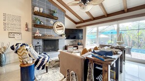 Un salon chaleureux avec une cheminée, un téléviseur et une grande fenêtre donnant sur un jardin.