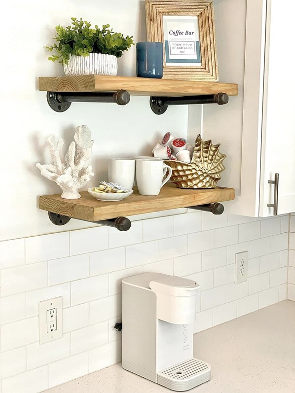 A kitchen with two wooden shelves holding a coffee bar sign, a potted plant, and various kitchen items. Below, there's a coffee maker on the countertop.