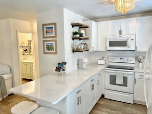 A modern kitchen with white cabinetry, a built-in microwave, a stove, and a coffee machine. There are framed pictures on the wall and a small island with a coffee maker.