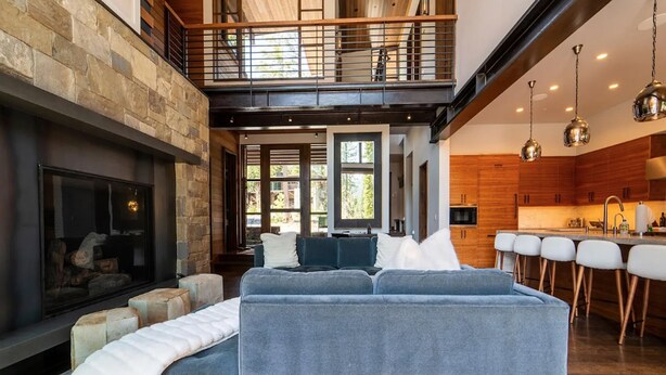 Una sala de estar moderna con chimenea, techo alto y zona de cocina con taburetes de bar.