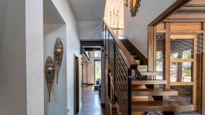 Un interior moderno con una escalera de madera, un largo pasillo y vistas a través de amplios ventanales.