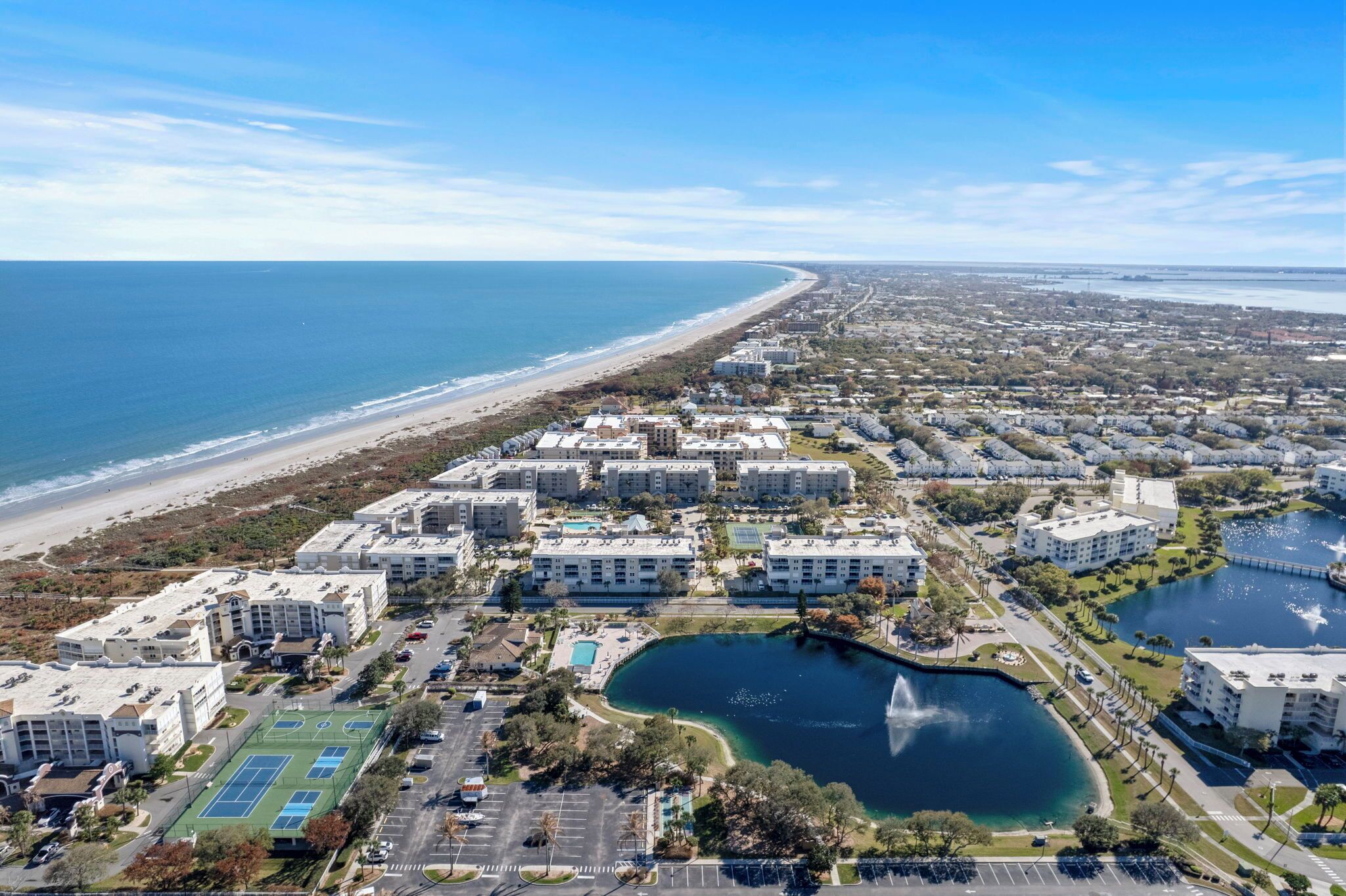 An aerial view of a coastal residential area with apartment buildings, a beach, and a lake.