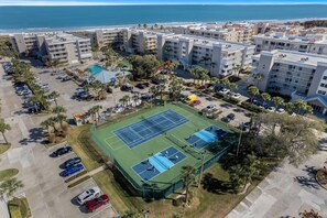 Vue aérienne d’un complexe hôtelier comprenant plusieurs bâtiments, un court de tennis et un parking.