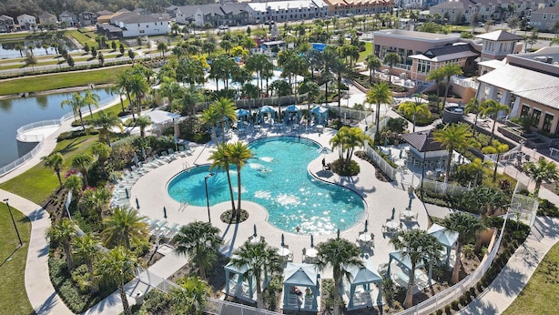 Een zwembad van een resort met palmbomen, ligbedden en een klein tuinhuisje.