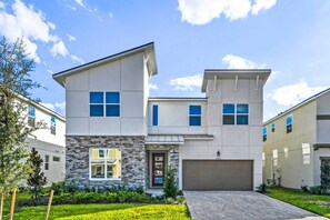 A modern two-story house with a stone facade, a garage, and a well-maintained lawn. - Private Pool Villa with Star Wars & Theater Fun (Kissimmee)