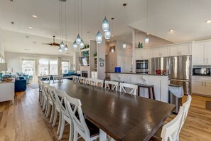 A spacious kitchen with a long wooden table, white chairs, and modern appliances.