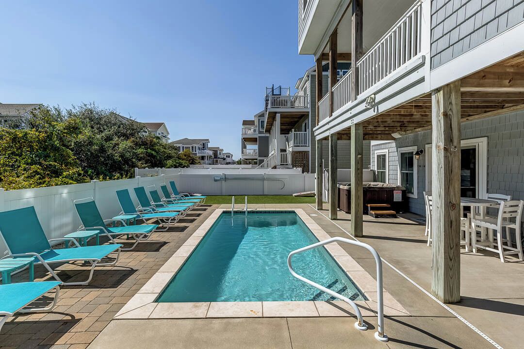 A swimming pool with lounge chairs, a covered patio area, and a view of other buildings.