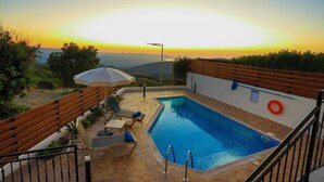 A swimming pool with a view of the sunset, wooden deck, and lounge chairs. - Villa Lefkas in Malatya (Meladeia)