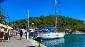 A marina with boats docked, a paved walkway, and a signboard with menu items. - Doras House in Gaios (Paxos)
