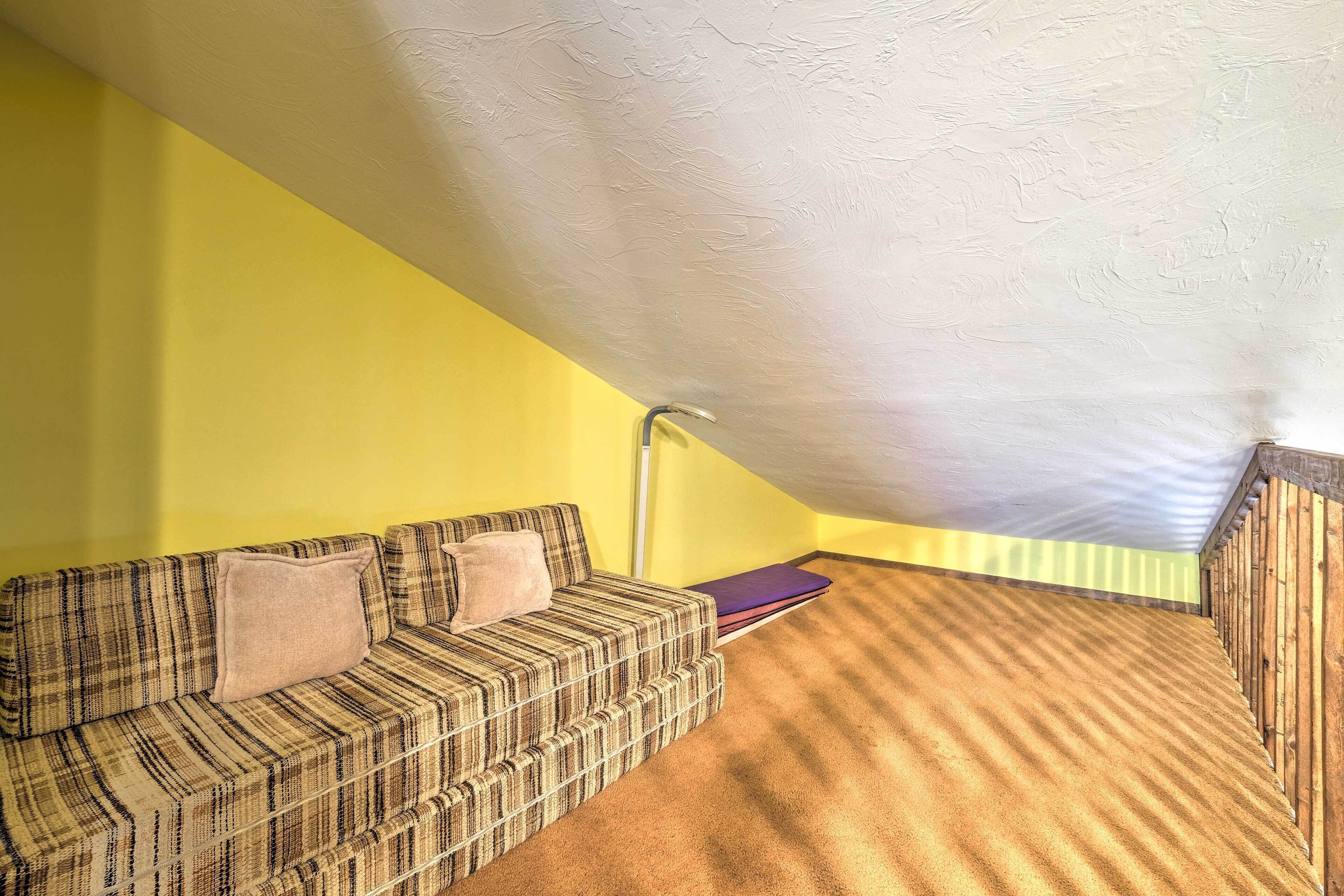 Een kamer met een schuine kap, een geruite bank met kussens en een houten vloer.