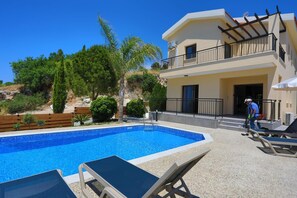 A poolside area with a clear blue pool, lounge chairs, and a building with a balcony. - Villa Melisos in Malatya (Meladeia)