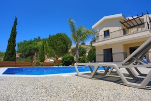 A pool area with lounge chairs, a clear blue sky, and a building with balconies overlooking the pool. - Villa Melisos in Malatya (Meladeia)