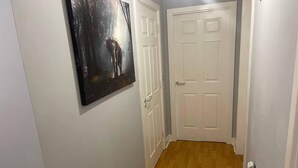 A hallway with a wooden floor, white walls, and a white door. There is a painting on the wall. - Remo Apartment Near Canary Wharf & 02 (London)