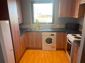 Cozinha compacta com armários de madeira, máquina de lavar embutida, fogão e janela com vista para o exterior.