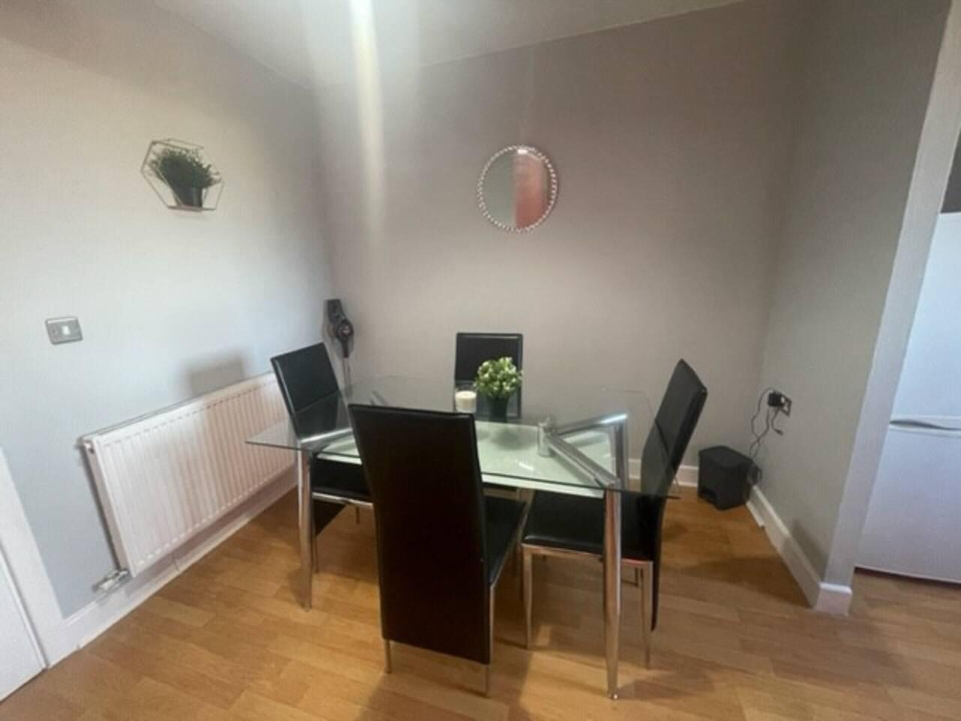 Een gezellig eetgedeelte met een glazen tafel, vier stoelen, een kleine plant in een pot en een spiegel aan de muur.