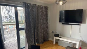 A modern living room with a large TV, a laptop, and a sofa. - Remo Apartment Near Canary Wharf & 02 (London)