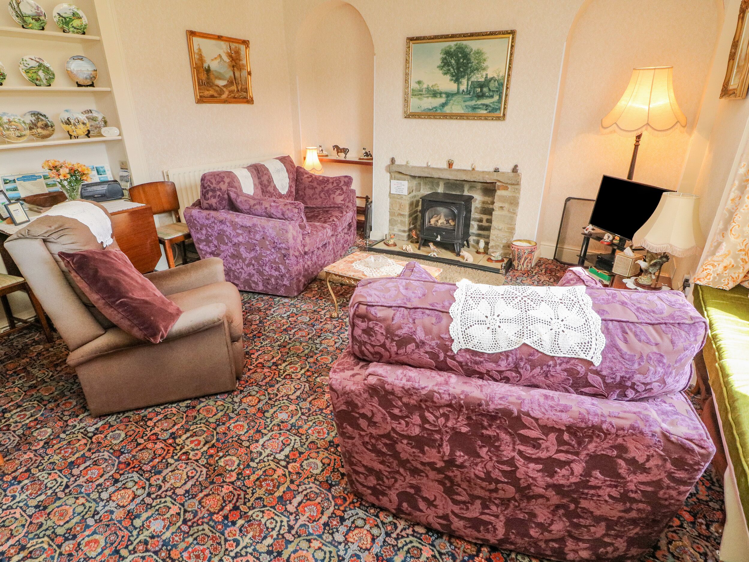 A traditional living room with patterned sofas, a fireplace, and decorative items on shelves.