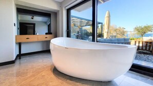 A modern bathroom with a large white bathtub, a wooden vanity with drawers, and a large window offering a view of the outdoors. - Çimentepe Residence Deluxe (Bodrum)