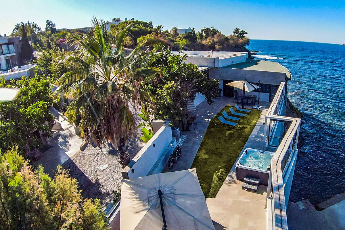 Una propiedad costera con piscina, mobiliario exterior y vista al mar.