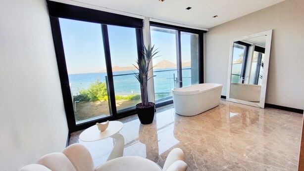 A modern bathroom with a large bathtub, a potted plant, and a view of the sea. - Çimentepe Residence Deluxe (Bodrum)