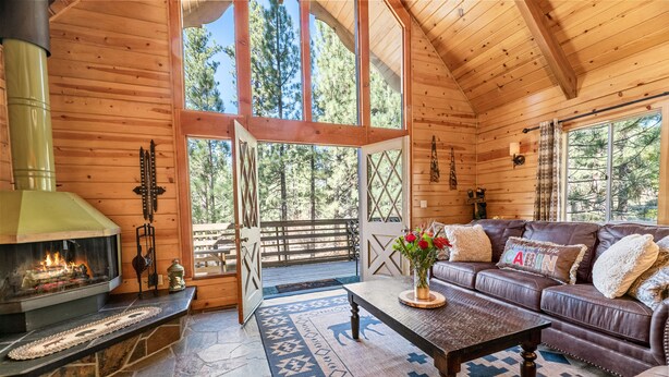 A cozy cabin interior with a stone fireplace, leather sofa, and large windows offering a view of the forest.