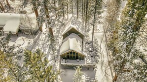 A snow-covered lodge with a central seating area and a covered porch, surrounded by dense forest.
