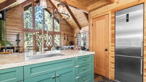 A kitchen with a stainless steel refrigerator, teal cabinets, and a stone-tiled floor.