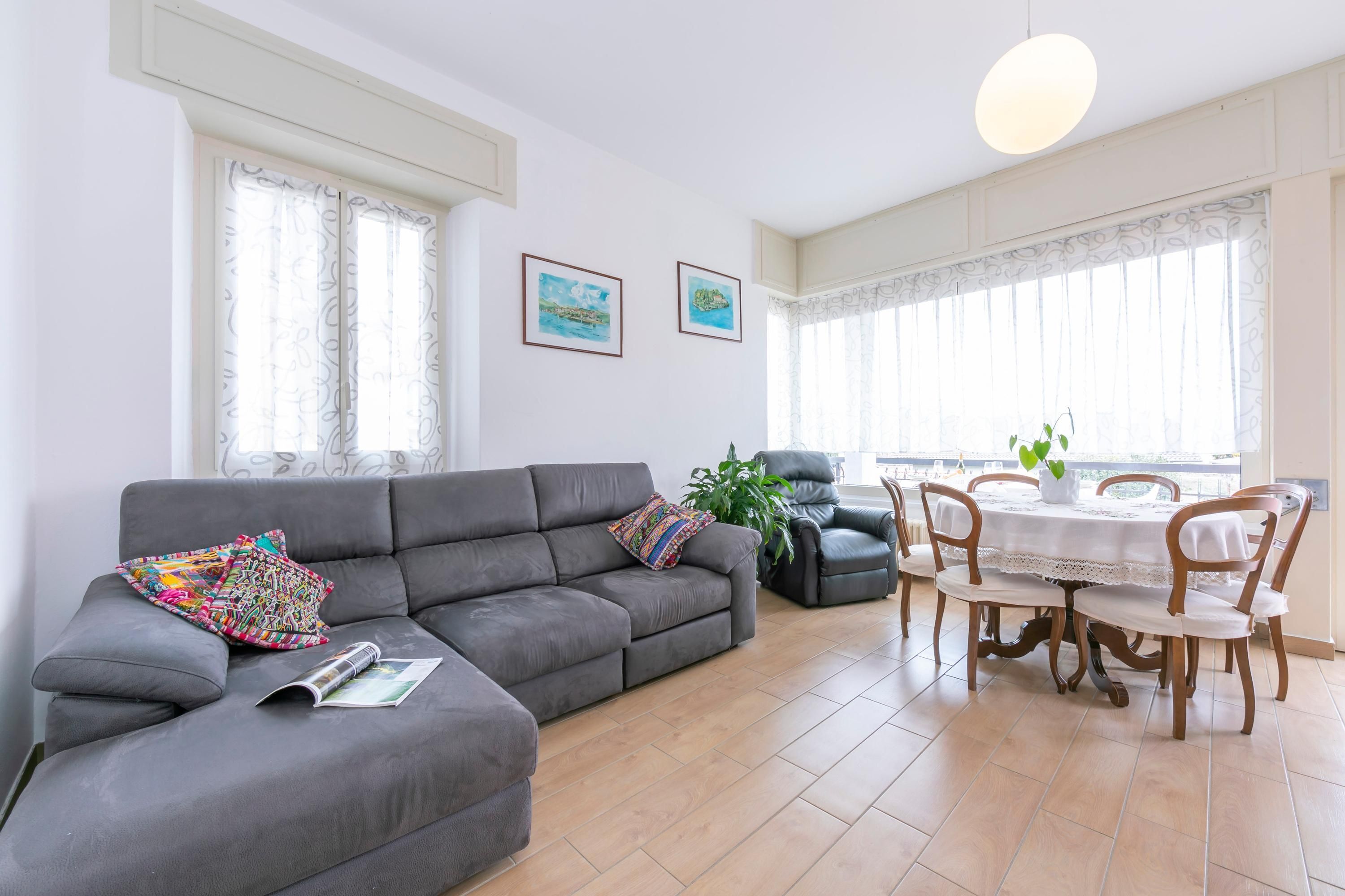 Una sala de estar con un sofá gris, una mesa de comedor con sillas y una planta en maceta.