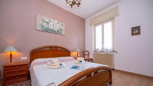 A bedroom with a wooden bed, bedside tables, a radiator, and a window with curtains.